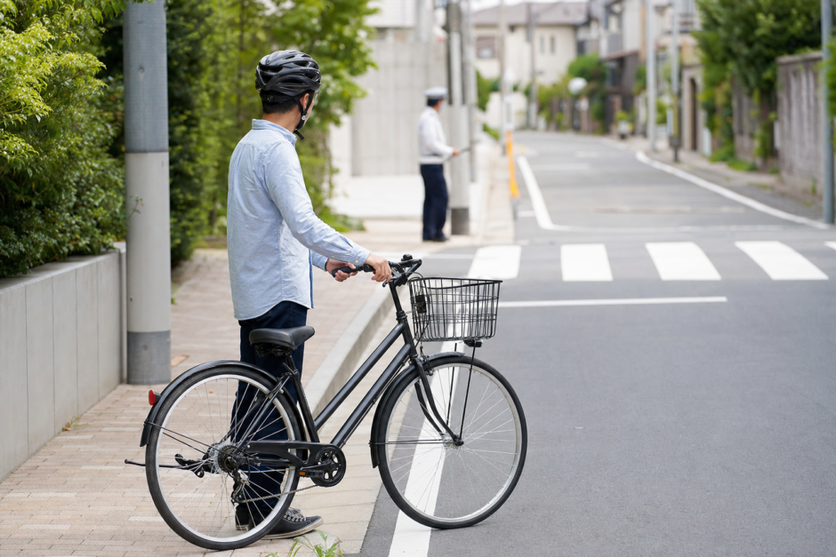 住宅街の横断歩道近くでヘルメットを着けた自転車利用者が安全な距離を取り落ち着いて確認している様子