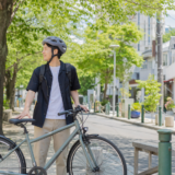 明るい街なかで自転車のそばに立つ利用者が無地の自転車用ヘルメットを正しく着用している様子