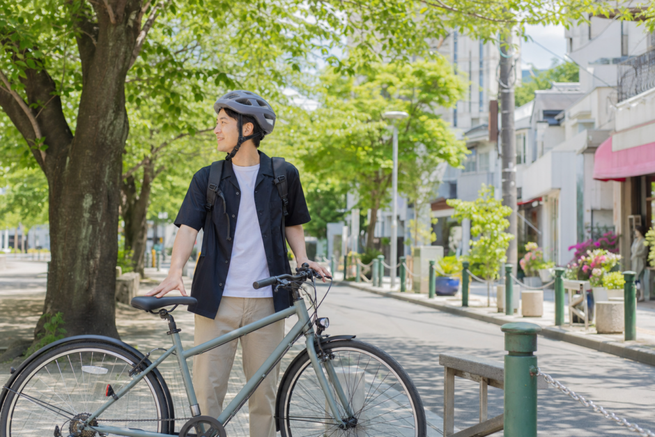 明るい街なかで自転車のそばに立つ利用者が無地の自転車用ヘルメットを正しく着用している様子