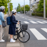 通学路の横断歩道手前でヘルメットを着用した保護者と生徒が自転車を止め、安全確認をしている様子