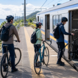 海の見える駅のホームでヘルメットを着用したサイクリストが自転車を安全に列車へ載せる準備をしている様子