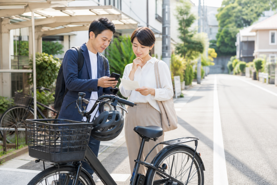 住宅街の明るい歩道脇でヘルメットを置いた自転車のそばに立つ親子が保険書類を確認している安全啓発イメージ