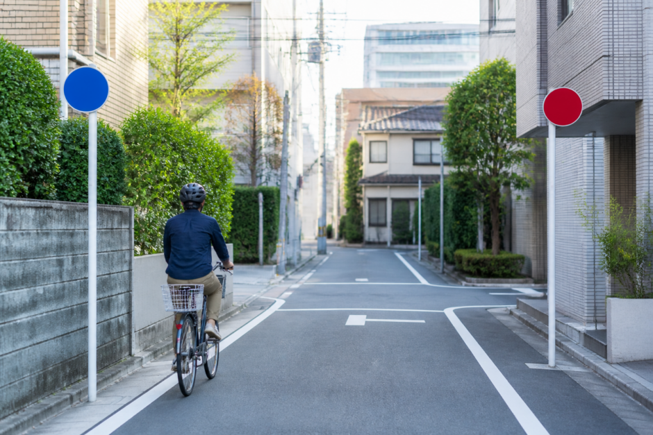 住宅街の一方通行路でヘルメットを着けた自転車利用者が左側を安全に走る様子