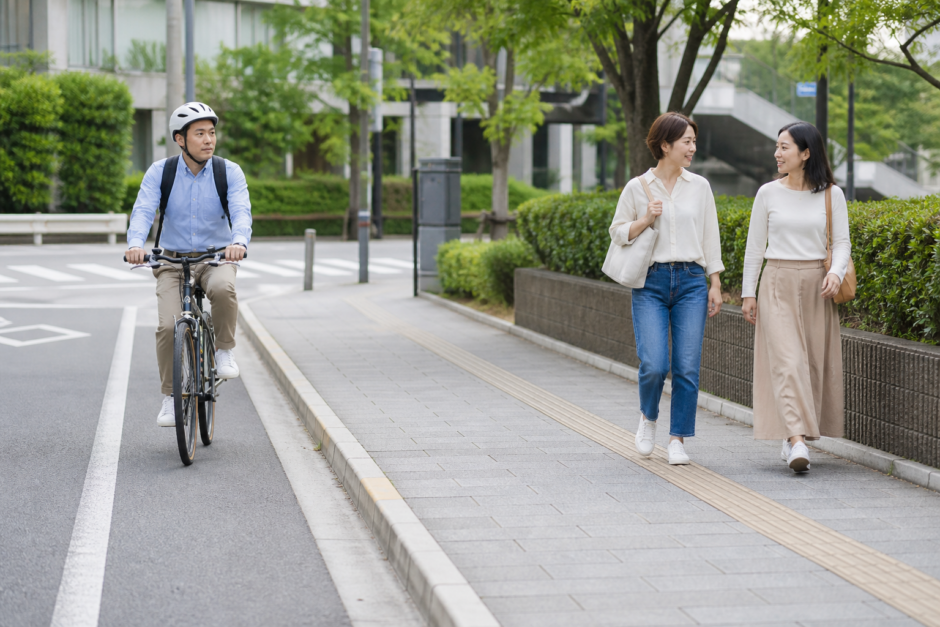 車道側を走るヘルメット着用の自転車利用者と歩道を歩く歩行者が十分な距離を取っている安全啓発イメージ
