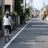 住宅街の道路左側にある路側帯付近をヘルメット着用の自転車利用者が安全に走る様子