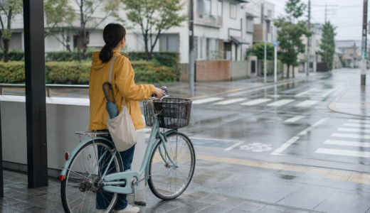 雨の日に傘を差さずレインウェアで自転車のそばに立ち周囲を確認する利用者