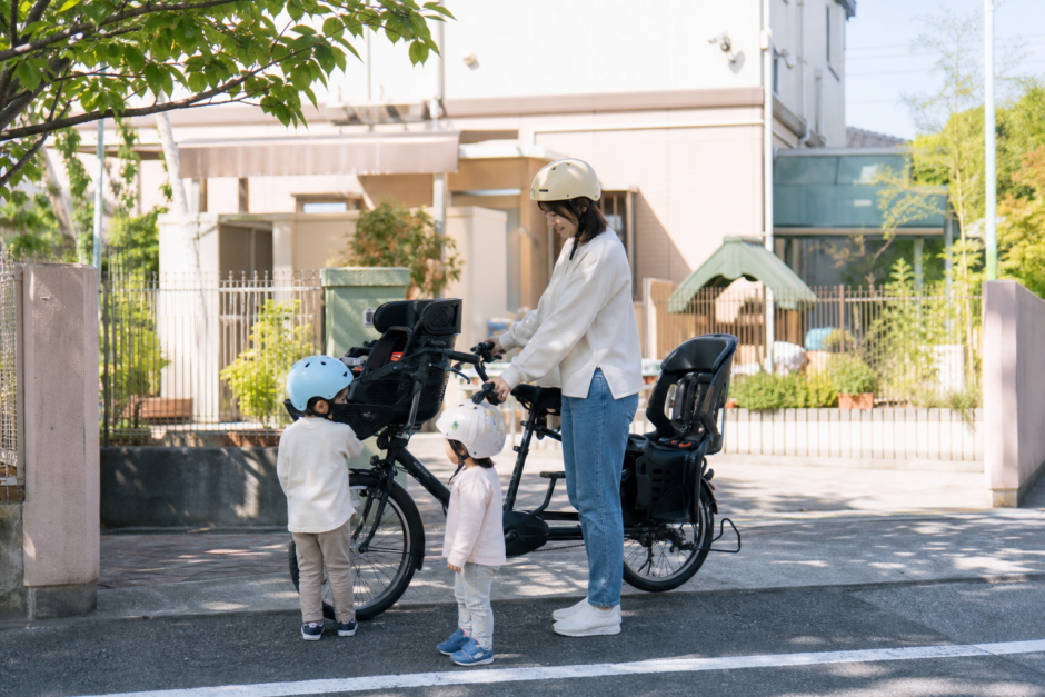 保育園前の静かな道でヘルメットを着けた子どもと子供乗せ自転車を確認する保護者
