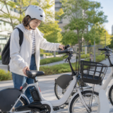 街角のシェアサイクルポートでヘルメットを着用した利用者が電動アシスト自転車のサドルを確認しているイメージ
