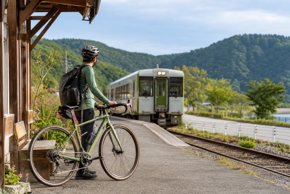 山あいの駅でヘルメットを着用したサイクリストが自転車を押し、列車を待つ花輪線サイクルトレイン旅のイメージ