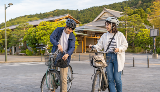 京都西山を思わせる駅前広場でヘルメットを着用した利用者がレンタサイクルを準備している明るい観光サイクリングのイメージ