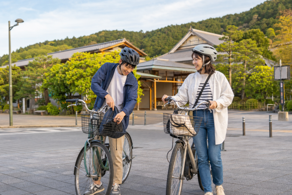 京都西山を思わせる駅前広場でヘルメットを着用した利用者がレンタサイクルを準備している明るい観光サイクリングのイメージ
