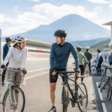 富士山を望むサーキットのピットエリアでヘルメットを着用した参加者が自転車イベントに向けて安全に準備している様子