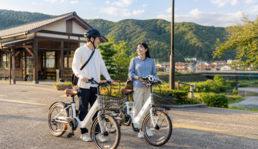 雲南市の里山に近い駅前でヘルメットを持った大人がシェアサイクルの電動アシスト自転車を準備しているイメージ