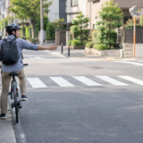 交差点手前で後方確認しながら手で合図を出すヘルメット着用の自転車利用者