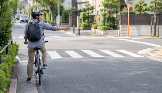 交差点手前で後方確認しながら手で合図を出すヘルメット着用の自転車利用者