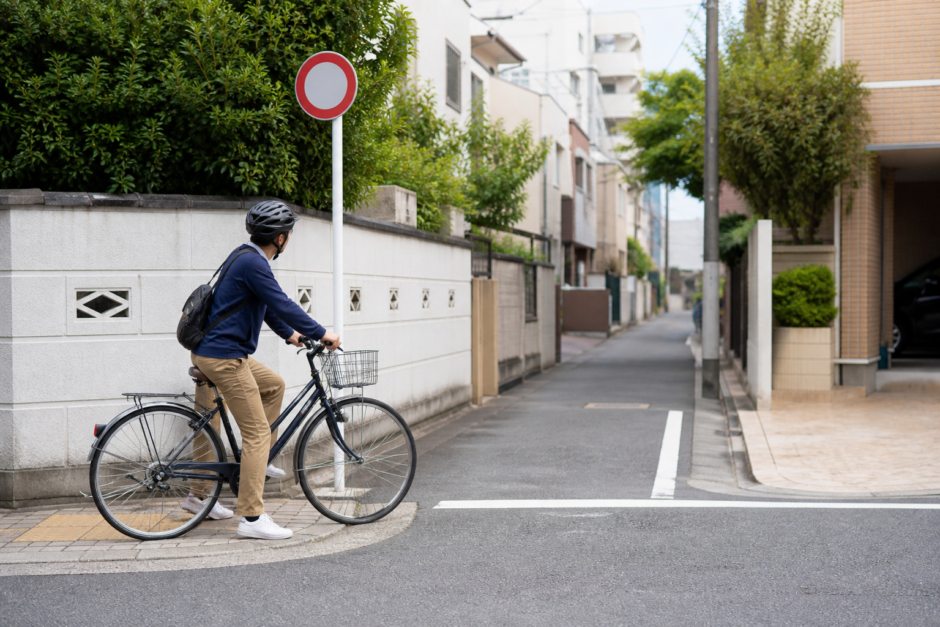 通行規制の標識の手前で止まり安全を確認するヘルメット着用の自転車利用者