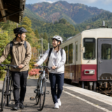 秋の山あいの駅でヘルメット姿のサイクリストが列車のそばで自転車を押している大糸線サイクルトレインのイメージ