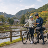 鯖街道沿線を思わせる里山の川沿いでヘルメット姿のサイクリストが安全に停車して地図を確認している秋の自転車旅イメージ