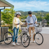 多賀サービスエリア近くのレンタサイクル拠点でヘルメット姿の利用者が自転車を確認している明るい観光サイクリングのイメージ