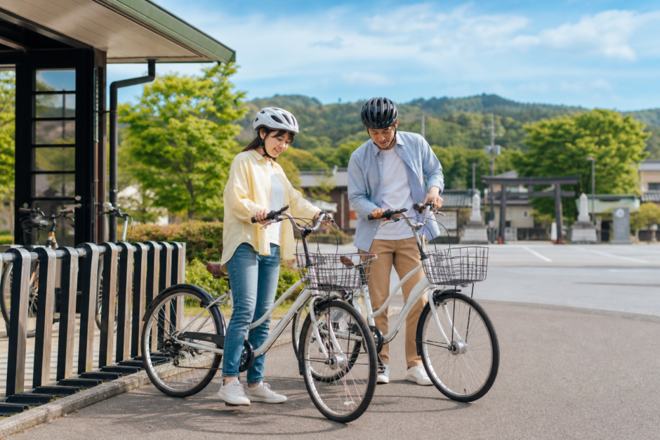 多賀サービスエリア近くのレンタサイクル拠点でヘルメット姿の利用者が自転車を確認している明るい観光サイクリングのイメージ
